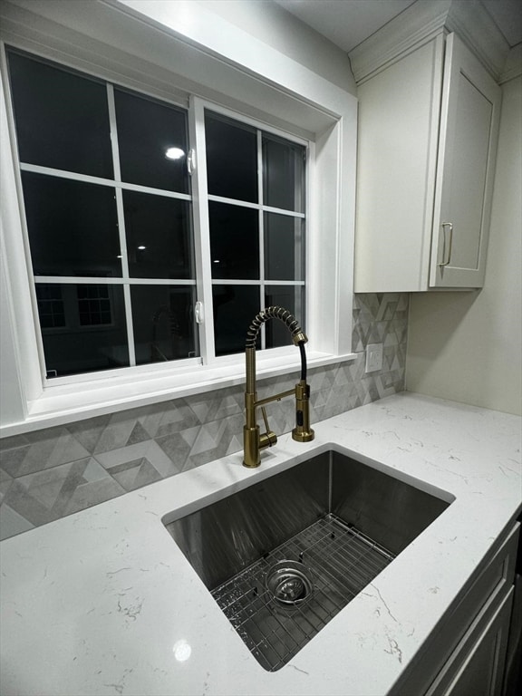 room details featuring tasteful backsplash, light stone countertops, sink, and white cabinets