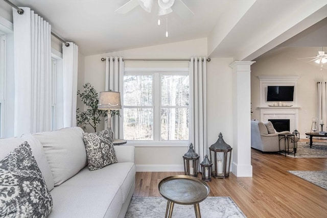 living room with ceiling fan, vaulted ceiling, a tile fireplace, light wood-type flooring, and decorative columns