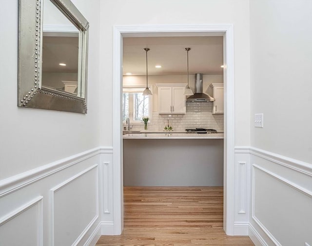 kitchen with decorative backsplash, hanging light fixtures, light wood-type flooring, white cabinets, and wall chimney exhaust hood