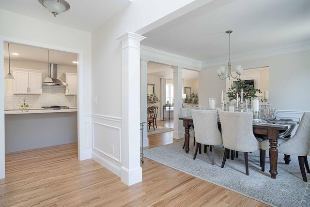 dining space featuring light hardwood / wood-style flooring, a notable chandelier, crown molding, and ornate columns