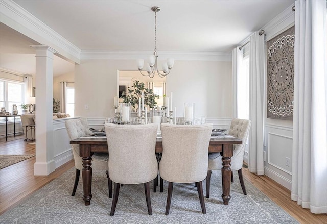 dining space with wood-type flooring, a notable chandelier, ornamental molding, and decorative columns