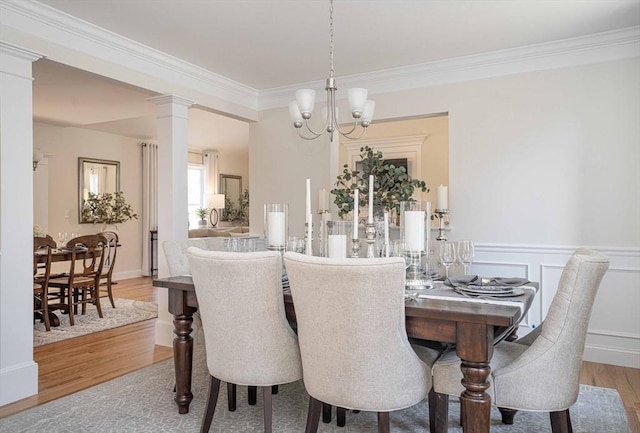 dining space with wood-type flooring, a notable chandelier, crown molding, and ornate columns