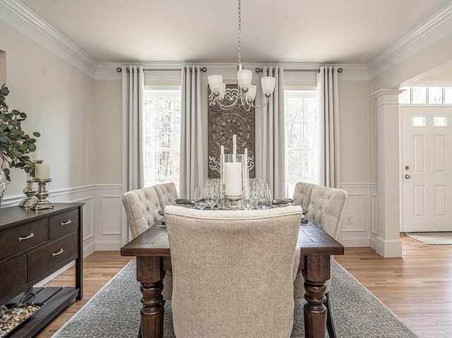 dining space featuring light hardwood / wood-style flooring, ornamental molding, ornate columns, and an inviting chandelier