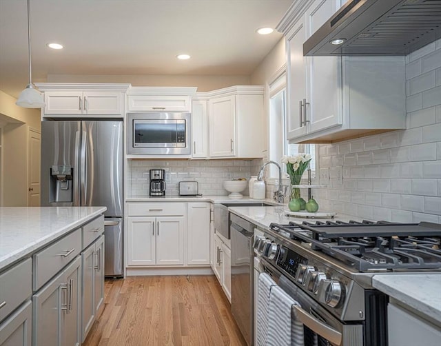 kitchen with light stone countertops, white cabinets, wall chimney exhaust hood, and stainless steel appliances