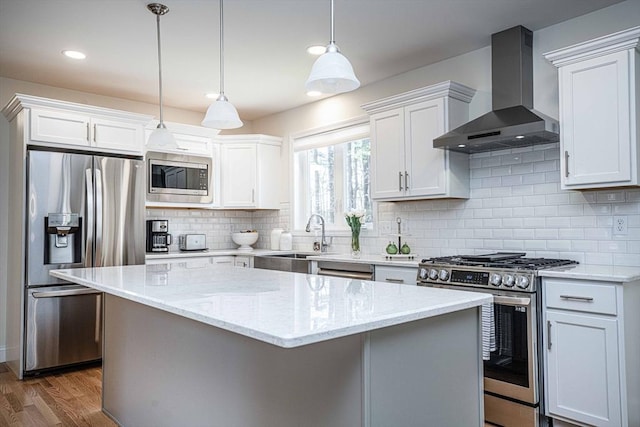 kitchen featuring white cabinetry, appliances with stainless steel finishes, wall chimney range hood, pendant lighting, and light stone counters