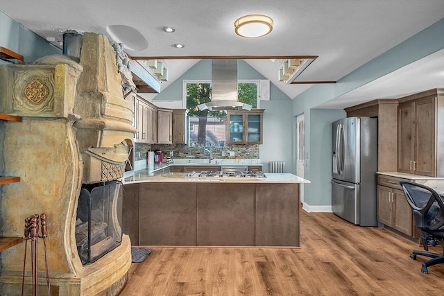 kitchen with backsplash, range hood, stainless steel fridge, a peninsula, and vaulted ceiling