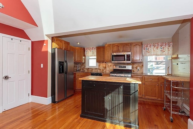 kitchen featuring brown cabinets, stainless steel appliances, light wood finished floors, decorative backsplash, and wooden counters