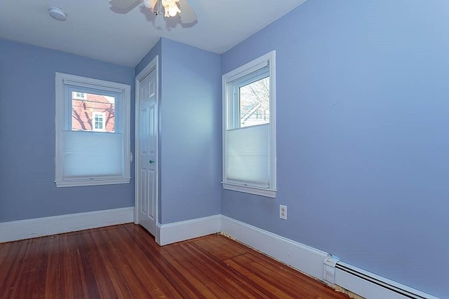 empty room with baseboards, baseboard heating, a healthy amount of sunlight, and wood finished floors