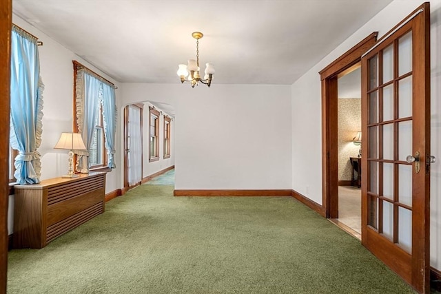 carpeted spare room with an inviting chandelier and french doors