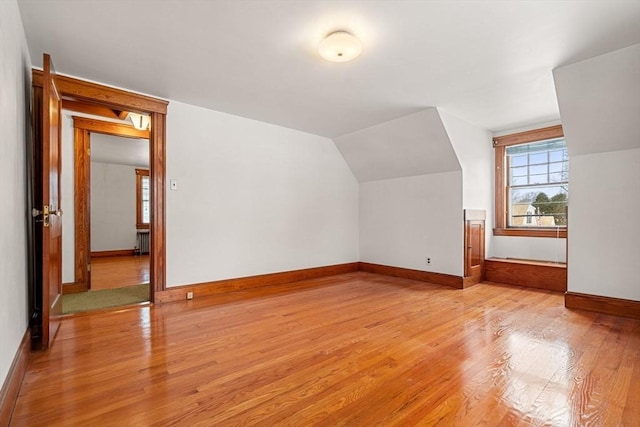 additional living space with lofted ceiling, radiator heating unit, and light wood-type flooring