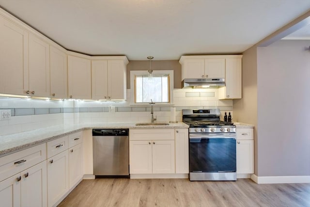 kitchen featuring sink, appliances with stainless steel finishes, hanging light fixtures, decorative backsplash, and light wood-type flooring