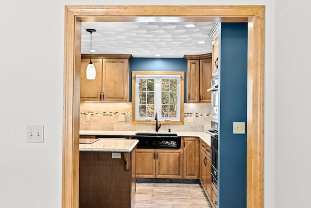 kitchen featuring light hardwood / wood-style flooring, tasteful backsplash, light stone counters, pendant lighting, and sink