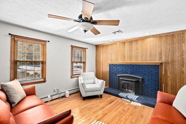 living room with wooden walls, ceiling fan, a baseboard heating unit, and hardwood / wood-style floors