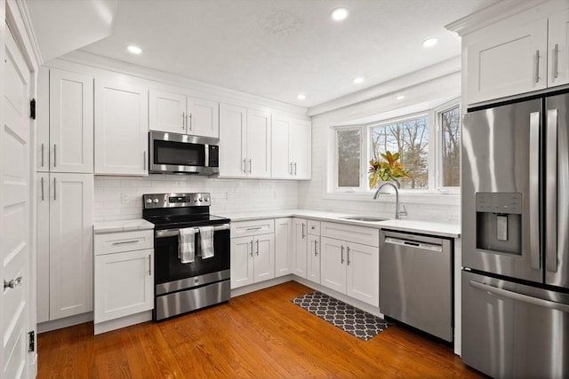 kitchen with sink, stainless steel appliances, backsplash, white cabinets, and hardwood / wood-style flooring