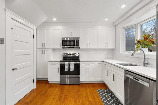 kitchen with decorative backsplash, appliances with stainless steel finishes, sink, light hardwood / wood-style flooring, and white cabinets