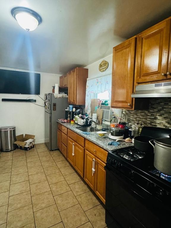 19 6th St, Chelsea, MA 02150 - kitchen with light tile patterned floors, freestanding refrigerator, black range with gas cooktop, backsplash, and under cabinet range hood
