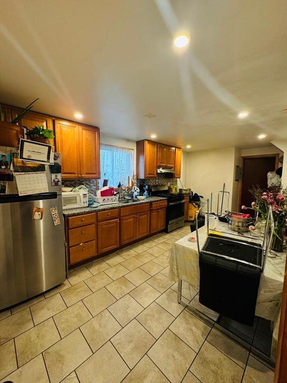 19 6th St, Chelsea, MA 02150 - kitchen with light tile patterned floors, stainless steel appliances, brown cabinetry, and tasteful backsplash