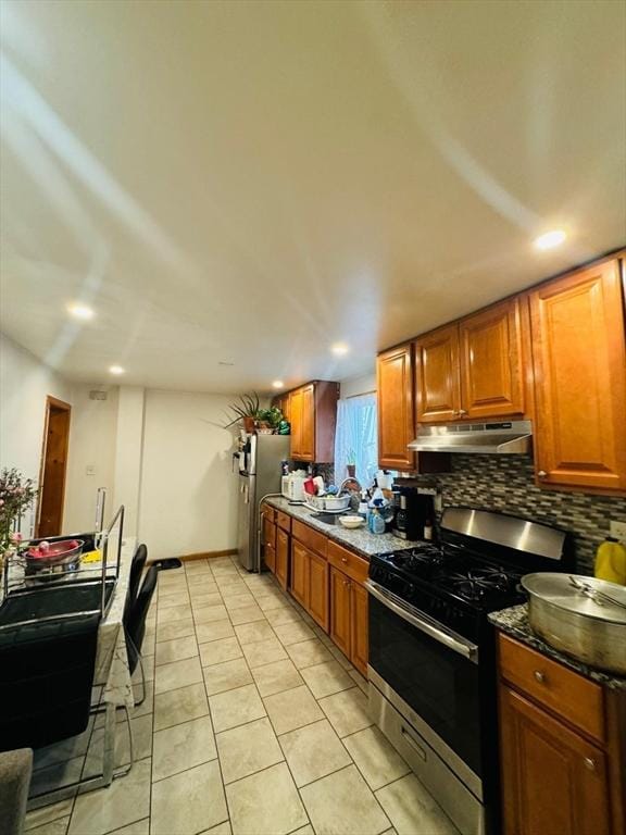 19 6th St, Chelsea, MA 02150 - kitchen featuring light tile patterned floors, brown cabinetry, under cabinet range hood, appliances with stainless steel finishes, and tasteful backsplash