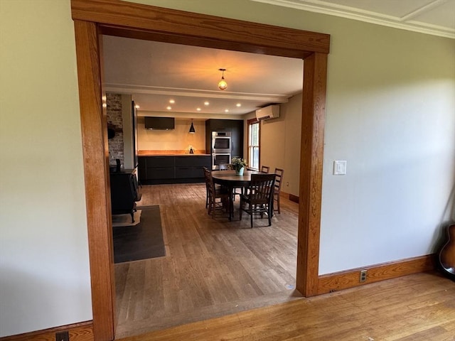 dining space with a wood stove, a wall unit AC, ornamental molding, and hardwood / wood-style floors