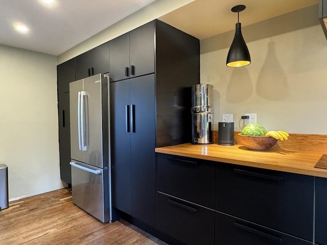 kitchen featuring wooden counters, light hardwood / wood-style floors, stainless steel refrigerator, and hanging light fixtures