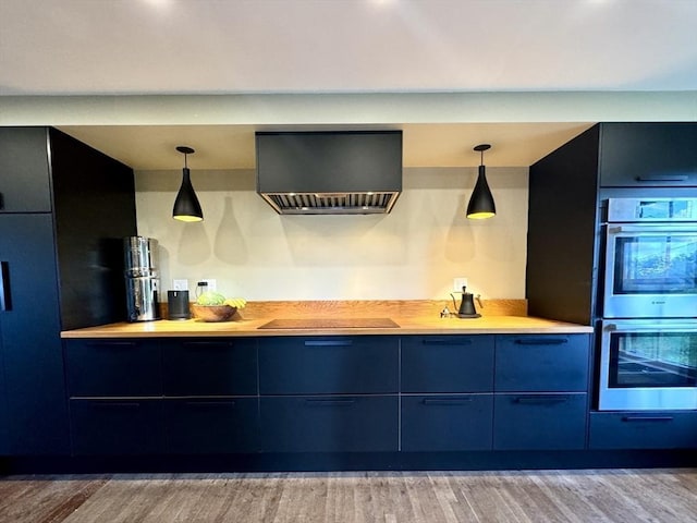 kitchen with black electric stovetop, stainless steel double oven, wall chimney range hood, wood-type flooring, and hanging light fixtures