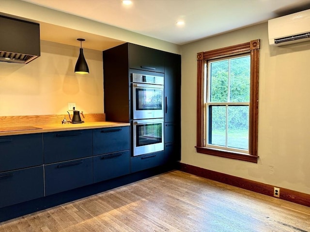 kitchen featuring blue cabinets, hanging light fixtures, light wood-type flooring, double oven, and a wall unit AC