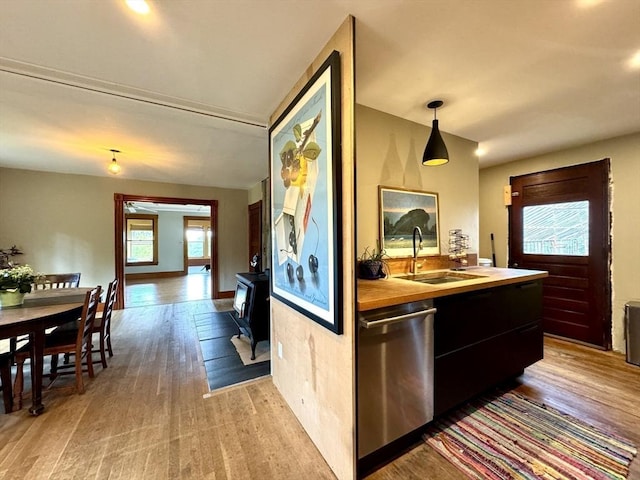 kitchen with sink, decorative light fixtures, light hardwood / wood-style flooring, dishwasher, and a wood stove