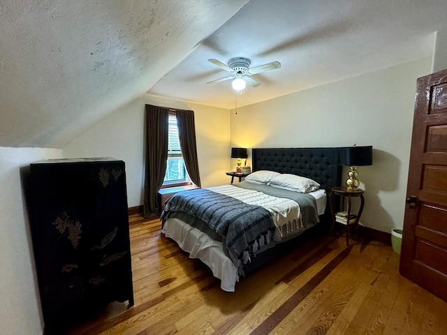 bedroom with hardwood / wood-style floors, a textured ceiling, vaulted ceiling, and ceiling fan