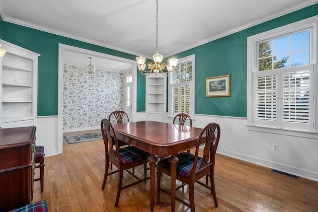 dining space featuring visible vents, baseboards, hardwood / wood-style flooring, crown molding, and a notable chandelier