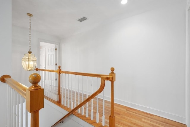 stairs with an inviting chandelier, baseboards, visible vents, and wood finished floors