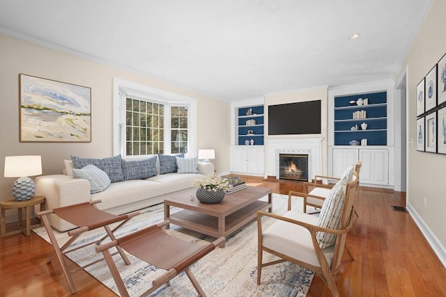 living room featuring a fireplace with flush hearth, crown molding, baseboards, and hardwood / wood-style flooring