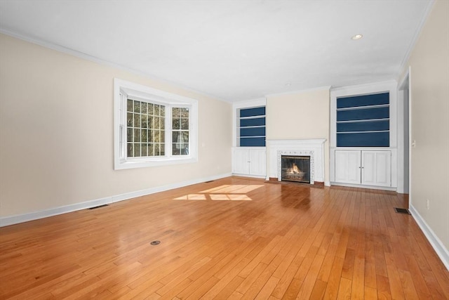 unfurnished living room with built in features, light wood-style flooring, ornamental molding, a fireplace with flush hearth, and baseboards