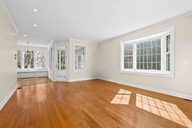 unfurnished living room with baseboards, crown molding, an inviting chandelier, and hardwood / wood-style flooring