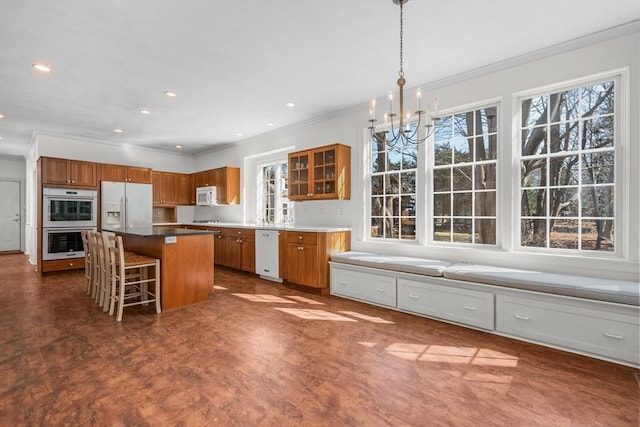 kitchen featuring white appliances, a breakfast bar, a kitchen island, brown cabinets, and glass insert cabinets