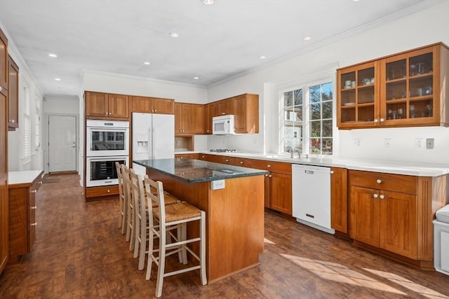 kitchen featuring a breakfast bar, a center island, brown cabinets, crown molding, and white appliances