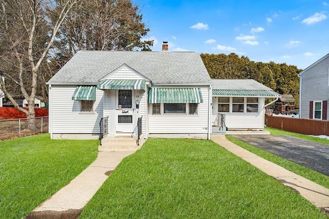 bungalow-style house with a shingled roof, a chimney, fence, and a front lawn