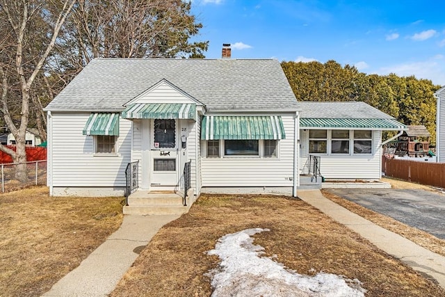 bungalow-style home with a shingled roof, a chimney, and fence