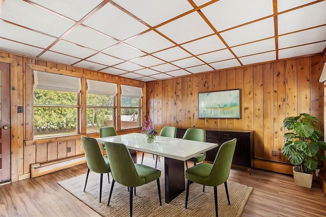 dining room featuring a baseboard heating unit, light wood finished floors, and wooden walls