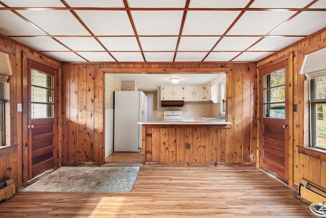 kitchen with wooden walls, white cabinets, light wood-style floors, range, and freestanding refrigerator