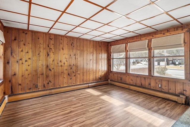 empty room with wooden walls, a baseboard heating unit, and wood finished floors