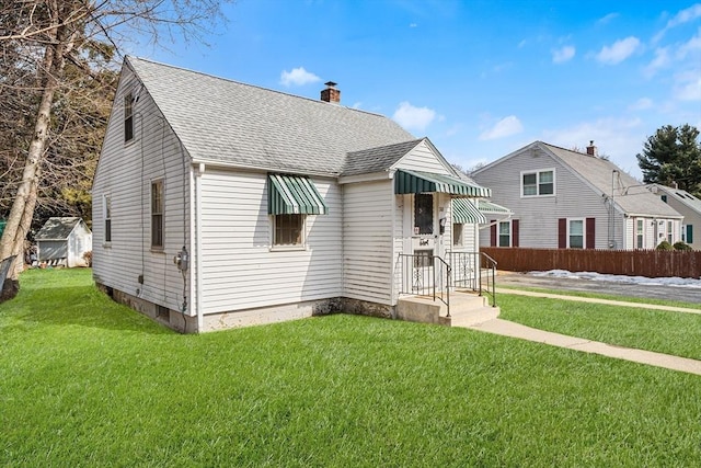 view of front of house featuring a shingled roof, a chimney, fence, and a front yard