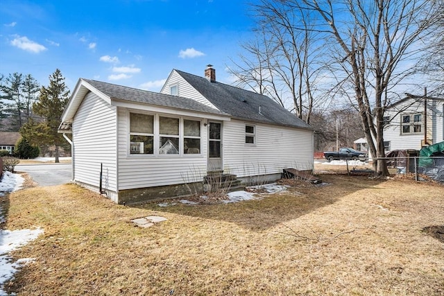 back of house with entry steps, a shingled roof, a chimney, and fence