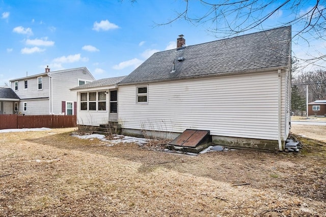 rear view of property featuring entry steps, a sunroom, a chimney, roof with shingles, and fence