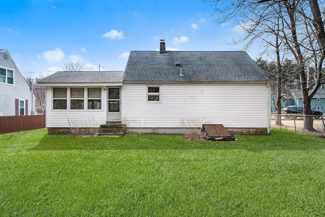 back of house with roof with shingles, a chimney, a lawn, entry steps, and fence