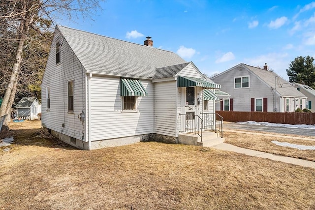 bungalow-style home with roof with shingles, fence, a chimney, and a front lawn