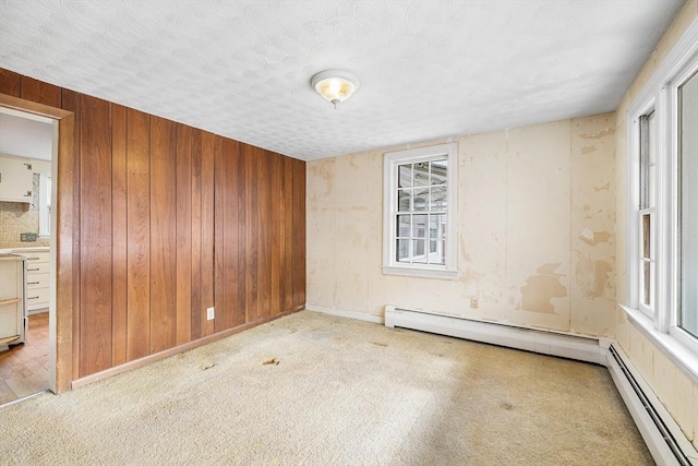 unfurnished room with carpet, wooden walls, baseboard heating, and a textured ceiling