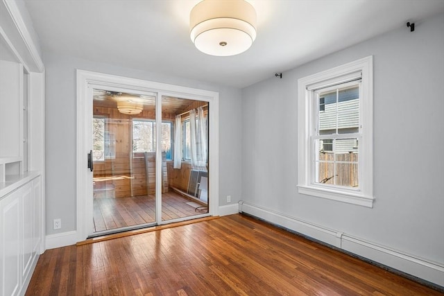 empty room featuring a baseboard heating unit, baseboards, and hardwood / wood-style floors