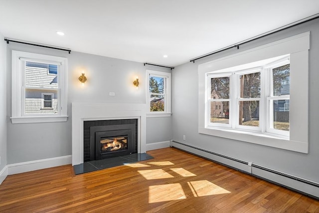 unfurnished living room featuring a fireplace with flush hearth, a healthy amount of sunlight, wood finished floors, and a baseboard radiator