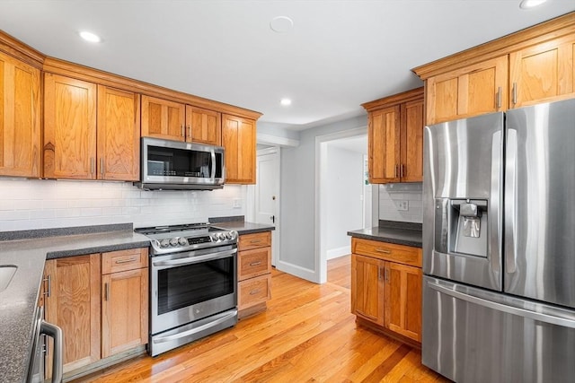 kitchen featuring brown cabinets, dark countertops, appliances with stainless steel finishes, and light wood finished floors