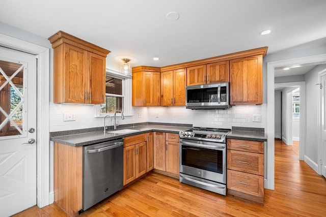 kitchen with a sink, stainless steel appliances, light wood-type flooring, and dark countertops